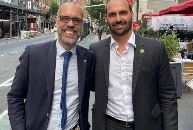 Allan dos Santos, ativista bolsonarista, tira foto sorrindo ao lado de Eduardo Bolsonaro em Nova Iorque.  Ambos usam terno - Metrópoles