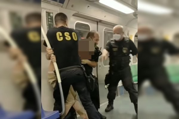 Homens com roupas pretas segurando homem com rosto borrado em vagão de metrô