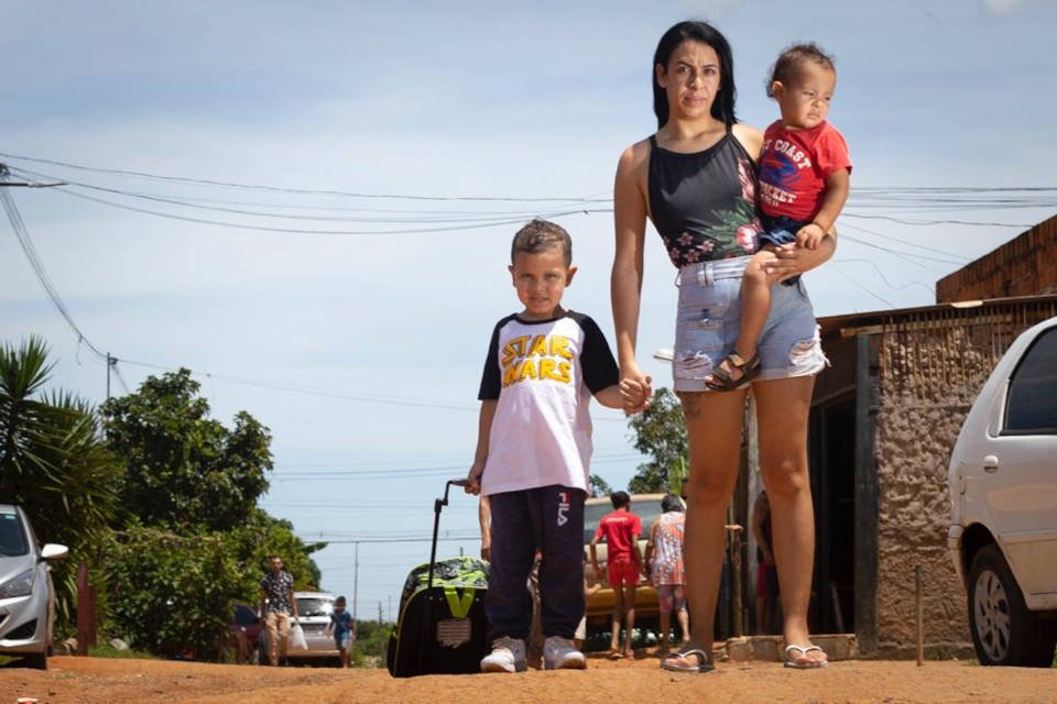 mulher em estrada com sol com duas crianças olhando para câmera