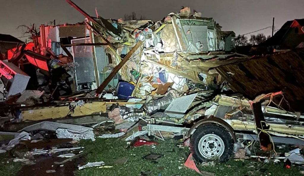 foto de um carro destruído e destroços de casas e outros objetos