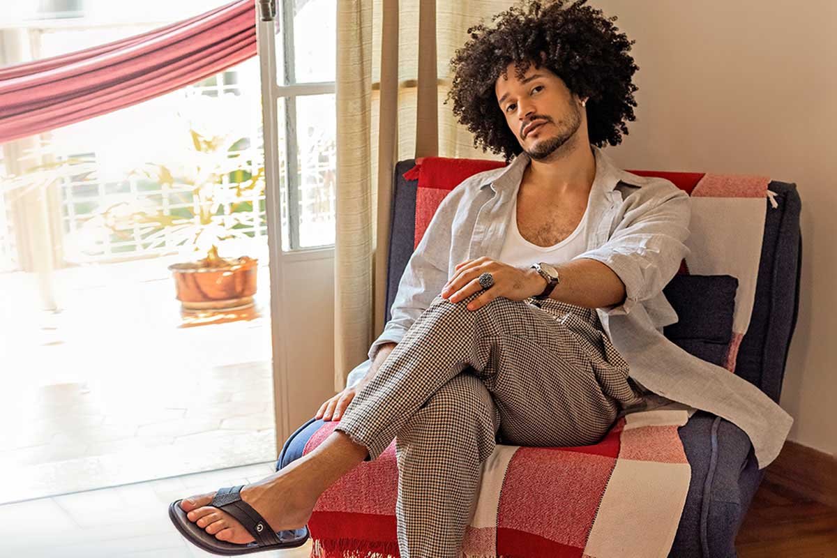 O influenciador digital Fabiano Gomes sentado em uma poltrona na sala com chinelo da marca Cartago