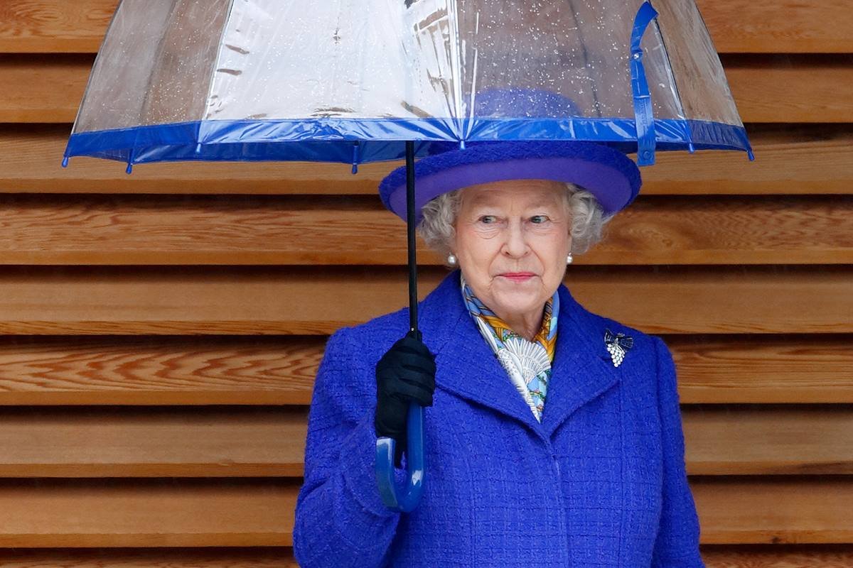 Foto colorida. Rainha Elizabeth com roupa azul e um guarda-chuva transparente