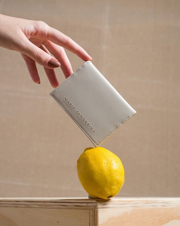 Carteira branca de couro vegano apoiada em um limão siciliano para foto de campanha da marca Maria Tangerina