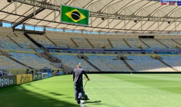 Homem com cortador de grama em campo de futebol com gramado verde