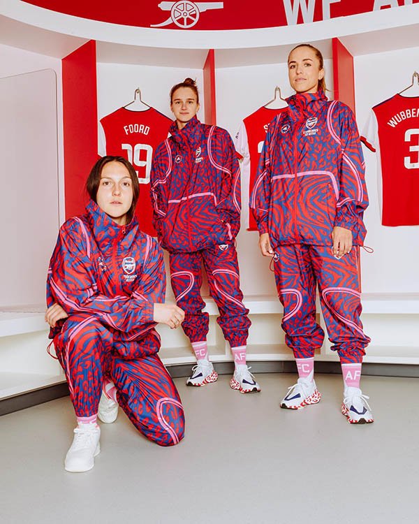 Jogadoras do time feminino inglês Arsenal com os novos uniformes desenhados pela parceria entre a Adidas e a estilista Stella McCartney. Na foto, elas estão no vestiário e usam os conjuntos de casaco e calça na mesma estampa.