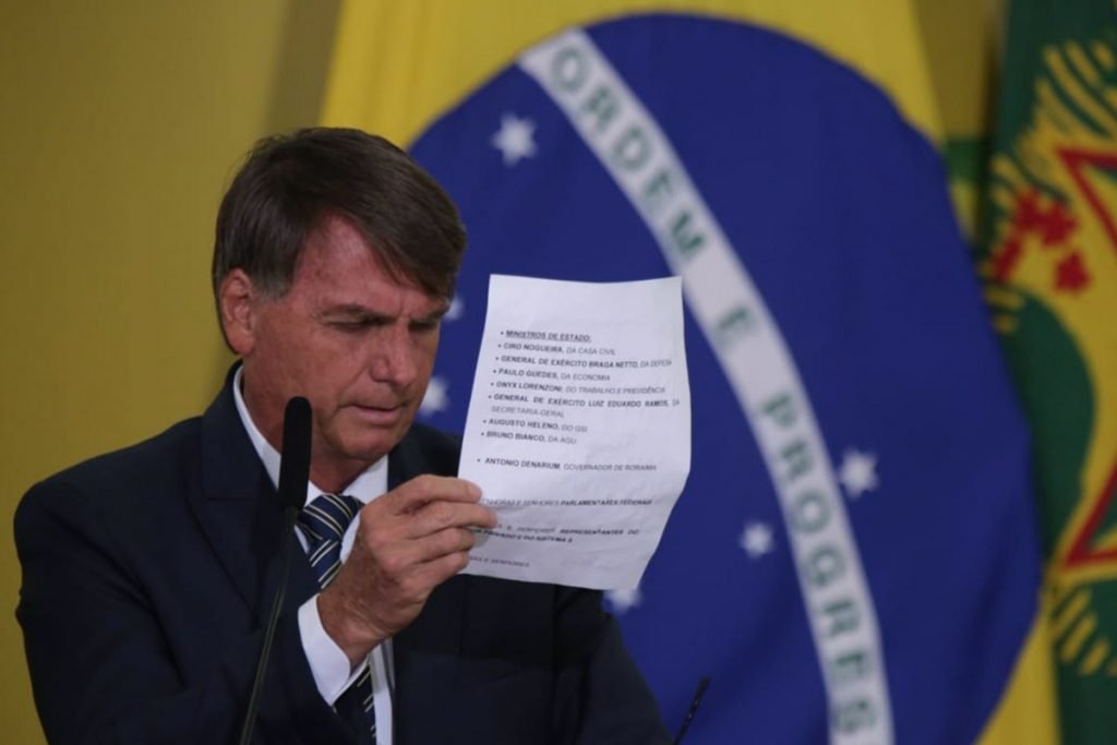 O presidente Bolsonaro lê discurso no Planalto no lançamento do Programa Renda e Oportunidade.  Ele usa terno e segurança folha de papel, frente ao microfone com a bandeira do Brasil ao fundo - Metrópoles