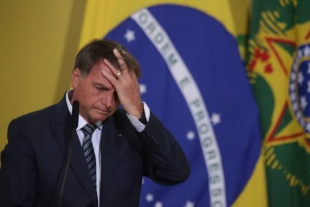 O presidente Bolsonaro em discurso no Planalto no lançamento do Programa Renda e Oportunidade. Ele usa terno e leva a mão a cabeça, frente ao microfone com a bandeira do Brasil ao fundo - Metrópoles