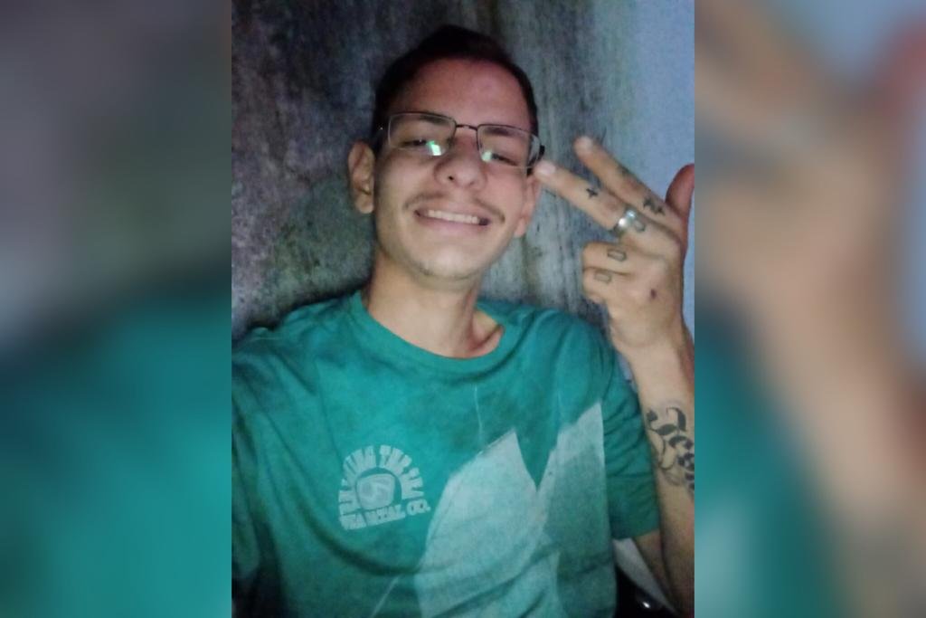 Jovem usando camiseta verde e óculos. Ele tem tatuagens no braço e mão- Metrópoles
