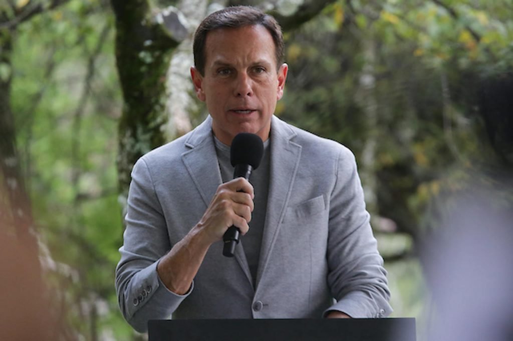 Governador de São Paulo, João Dória discursa em dia de liberação das máscaras em espaços fechados no estado. Ele usa terno cinza e fala ao microfone - Metrópoles