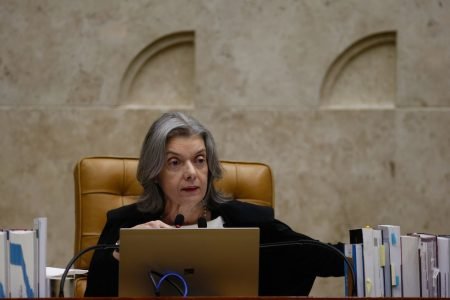 Ministra do STF, Camen Lucia, em votação do habeas corpus de Lula. Ela fala diante de um computador e microfones, cercada de livros - Metrópoles