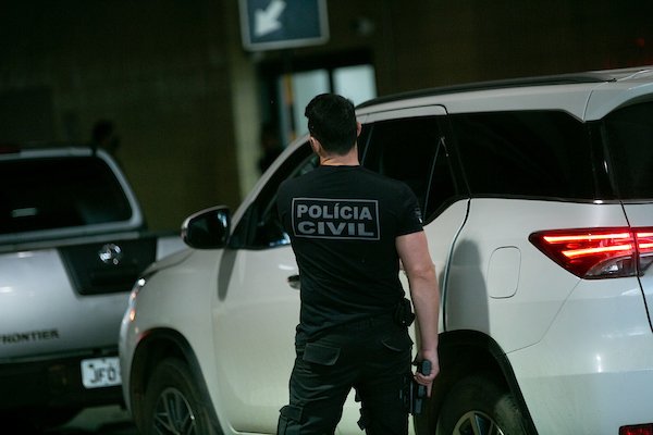 Foto colorida de policial civil de costas em frente a viatura
