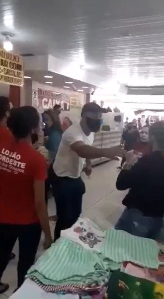 homem de amiseta branca coloca mão em ombro de vendedora