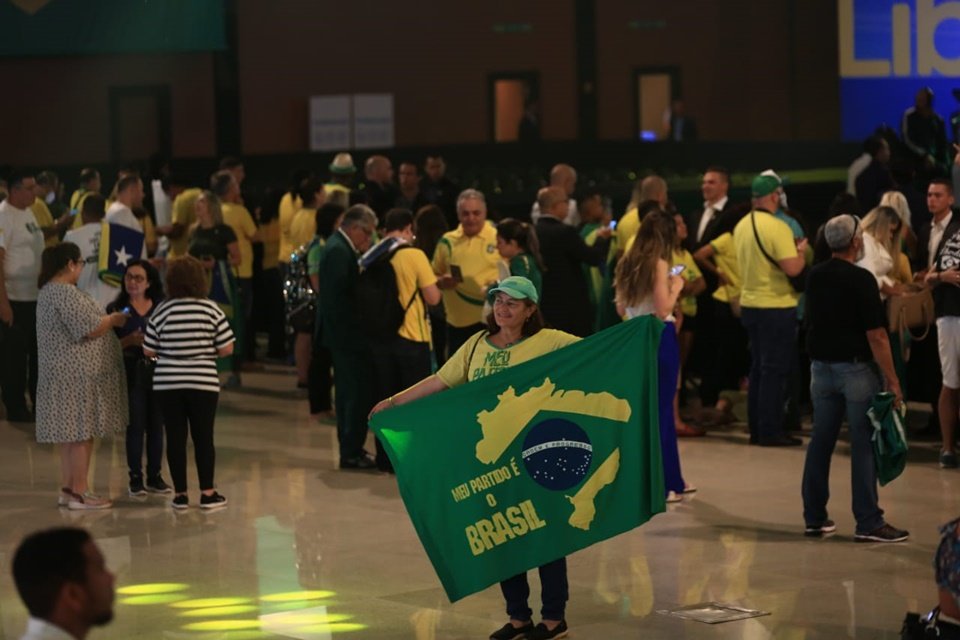 Em meio a uma multidão escrita, mulher segura uma bandeira com núcleos do Brasil onde: 
