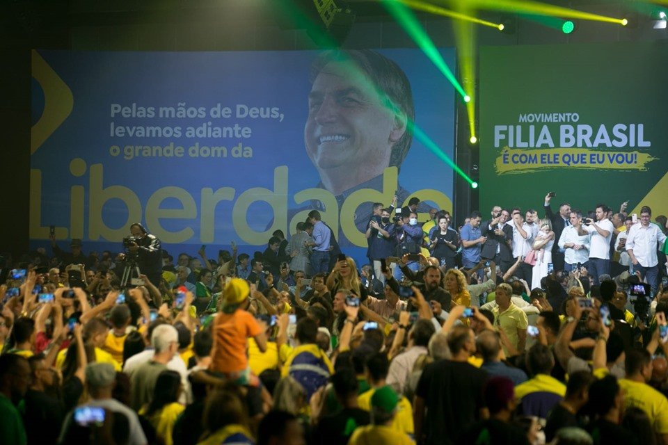 Multidão assiste a pessoas subindo no palco.  No meio, o presidente Jair Bolsonaor