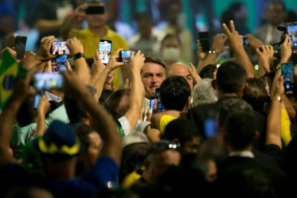 Presidente Jair Bolsonaro aparece em destaque em meio a uma multidão segurando celulares