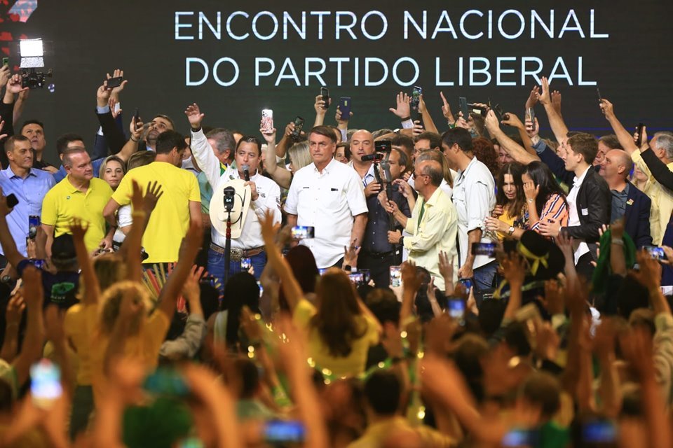 Diversas pessoas levantam o braço em direção ao presidente Jair Bolsonaro. Ao fundo, a frase: Encontro Nacional do Partido Liberal