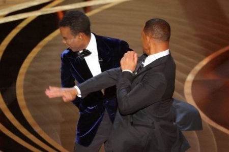 A imagem colorida mostra o ator Will Smith dando um tapa no rosto de Chris Rock, também ator, no palco do Oscar 2022