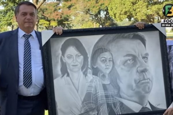 Bolsonaro segura quadro com desenho de sua família em frente ao palácio da Alvorada. O autor do quadro e apoiador do presidente segura do outro lado, só aparecendo suas mãos - Metrópoles