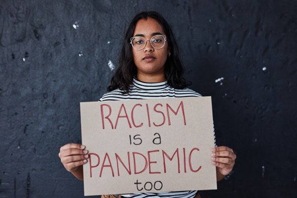 Pessoa segurando cartaz com palavras racismo também é uma pandemia em inglês