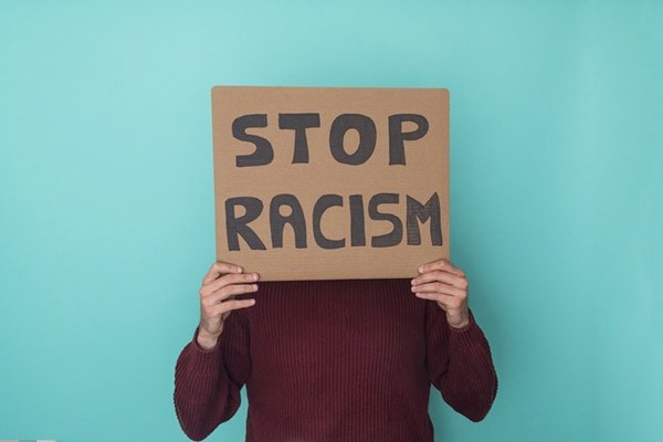 Pessoa segurando cartaz com palavras chega de racismo em inglês