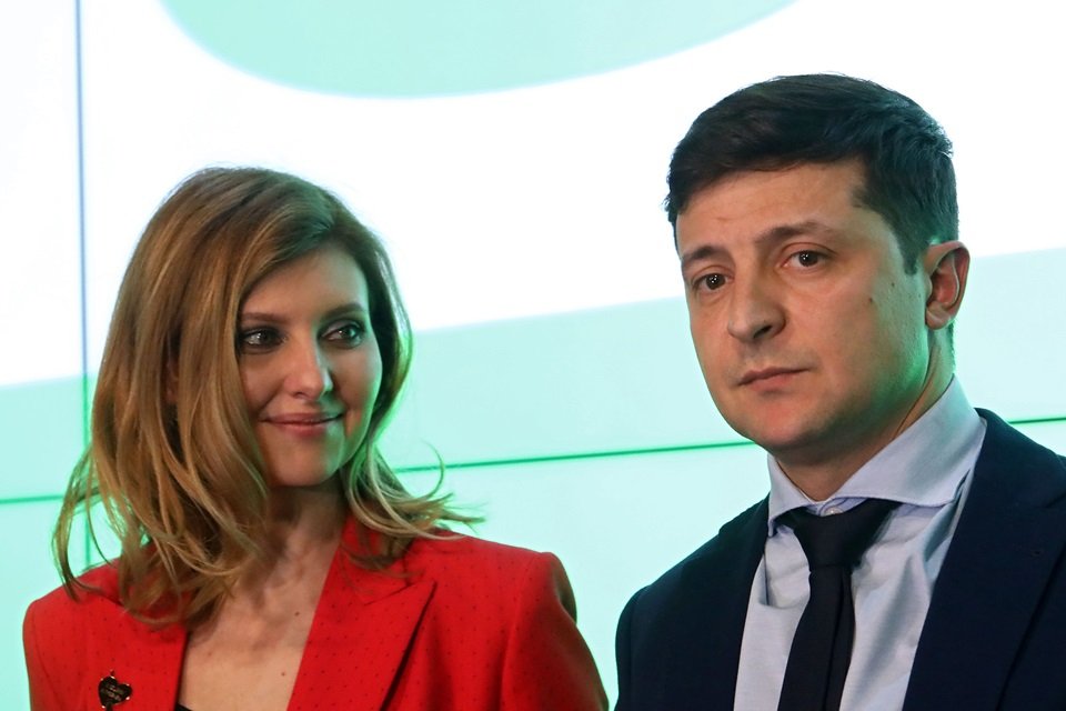 A primeira-dama da Ucrânia, Olena Zelenska, com roupas vermelhas ao lado do marido, o presidente Zelensky, de terno. Ela sorri para o marido - Metrópoles
