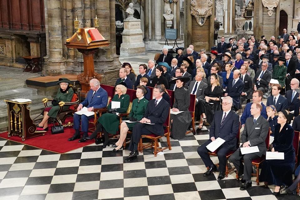 Foto colorida. Rainha Elizabeth e integrantes da família real sentados em uma igreja 