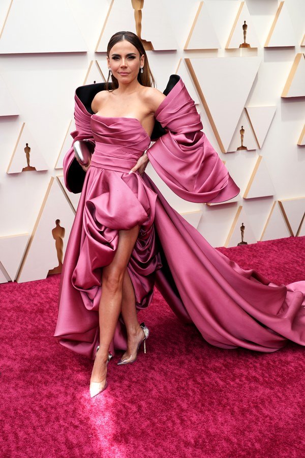 A cantora e atriz Carolina Gaitán no tapete vermelho do Oscar. Ela é uma mulher branca com cabelo longo e liso e usa um vestido rosa com cauda e mangas bufantes da marca Tony Ward