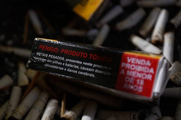 Foto de carteira de cigarro amassada jogada sob vários cigarros usados e queimados, com cinzas por cima - Metrópoles