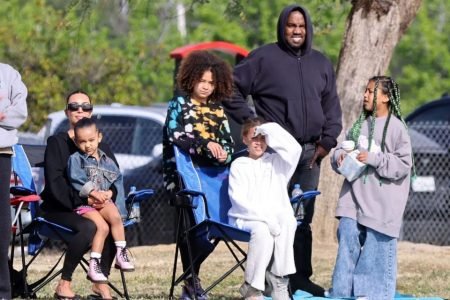 Foto colorida de Kanye West, Kim Kardashian e os filhos. Imagem de uma família e eles estão reunidos na beira de um campo de futebol - Metrópoles