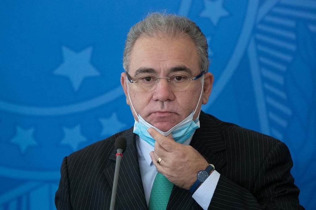 O ministro da Saúde, Marcelo Queiroga, abaixa a máscara durante fala em evento no Palácio do Planalto, sob fundo azul - Metrópoles