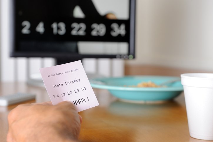 Pessoa olhando bilhete de loteria enquanto aparece números na tv - Metrópoles
