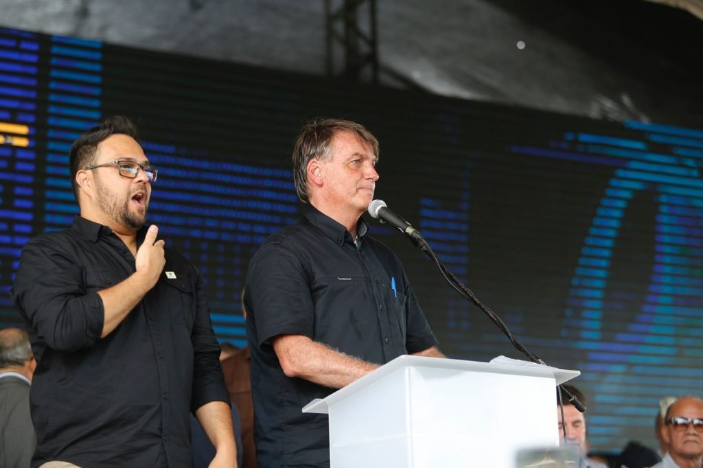 Em Parnamirim (RN) o presidente Bolsonaro discursa em pulpito, de camisa social preta. Ao lado, um tradutor de libras também usa roupa preta e ainda é possível ver um telão ao fundo - Metrópoles