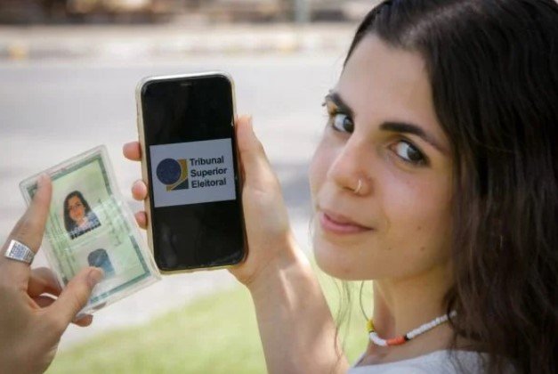 Mulher segurando identidade em uma mão e um celular na outra– Metrópoles
