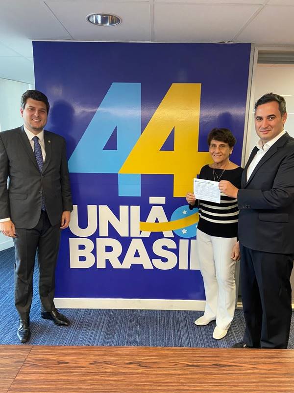 A política Eliana Pedrosa segura sua ficha de filiação ao União Brasil ao lado do presidente da legenda do DF. Ao fundo, um banner com o número da sigla - Metrópoles