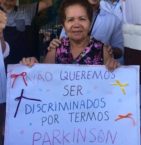 mulher idosa segura cartaz na cor branca com escritos sobre Parkinson