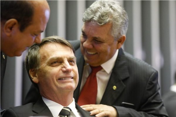 Os então deputados Alberto Fraga (em pé) e Jair Bolsonaro (sentado) na mesa diretora do plenário da Câmara dos Deputados. Ambos sorriem - Metrópoles