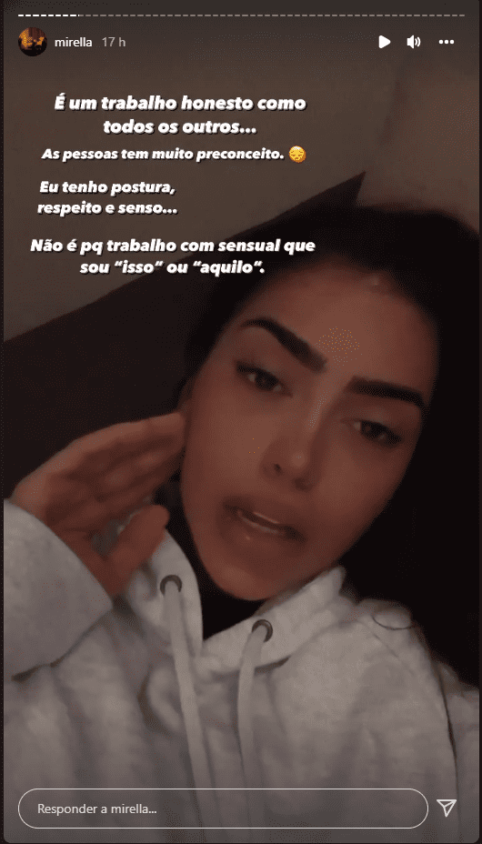 Mulher deitada em sofá, falando para a câmera, de casaco branco