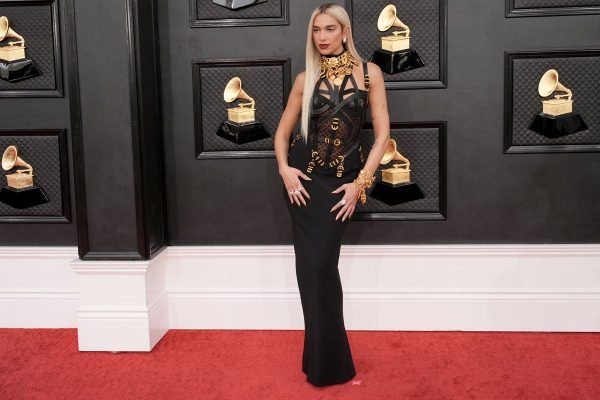 Dua Lipa, no tapete vermelho do Grammy 2022, usando vestido preto colado e longo, com detalhes dourados - Metrópoles