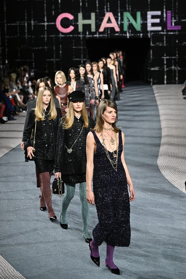 Fila final de desfile da marca Chanel. A coleção apresentada é a de outono/inverno de 2022 e a maioria das modelos usa roupas pretas, meia calça e sapatilhas