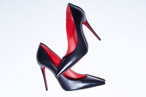 Salto alto fino, modelo Scarpin, da marca Louboutin. O sapato é preto com o solado e a parte interna vermelhos