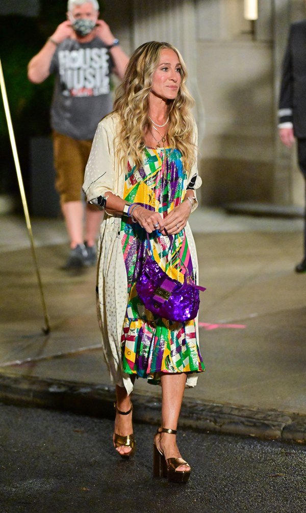 A atriz Sarah Jessica Parker nas ruas de Nova York durante a gravação da série "And Just Like That...". Ela usa um vestido colorido gráfico, um kimono branco com glitter, uma bolsa Baguette roxa de lantejoulas da Fendi e salto alto dourado.