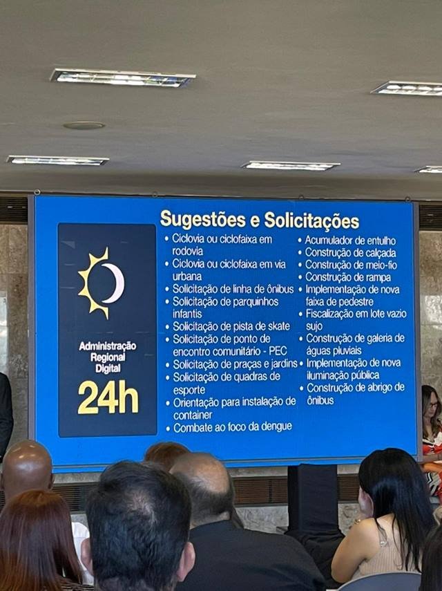 Painel azul com informações do GDF em cerimônia no Palácio do Buriti, com canais de atendimento da população com administração regional - Metrópoles
