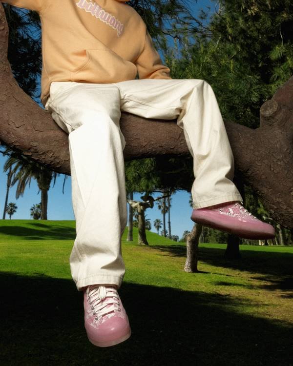 Pernas de homem sentado em tronco de árvores usando tênis rosa com estampa de cobra