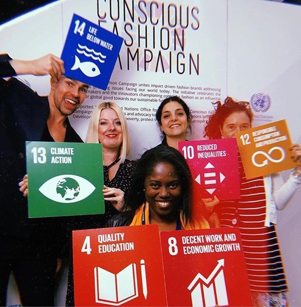 Pessoas segurando plaquinhas com os Objetivos de Desenvolvimento Sustentável da Organização das Nações Unidas (ONU). Na foto estão presentes um homem e quatro mulheres