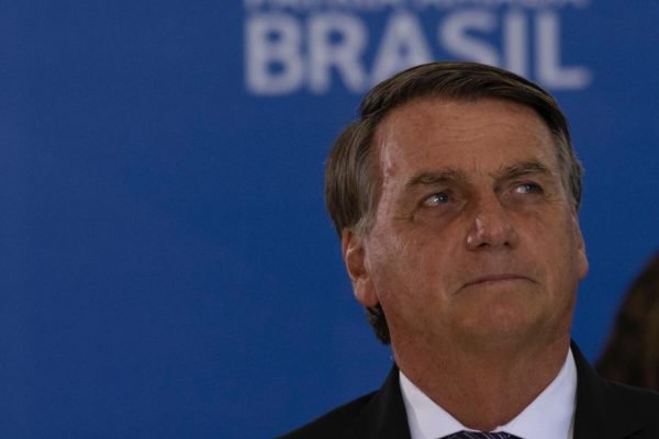 O presidente Bolsonaro cumprimenta os Oficiais-Generais promovidos na cerimônia realizada no palácio do Planalto. Ele olha para cima frente ao palco com fundo azul - Metrópoles