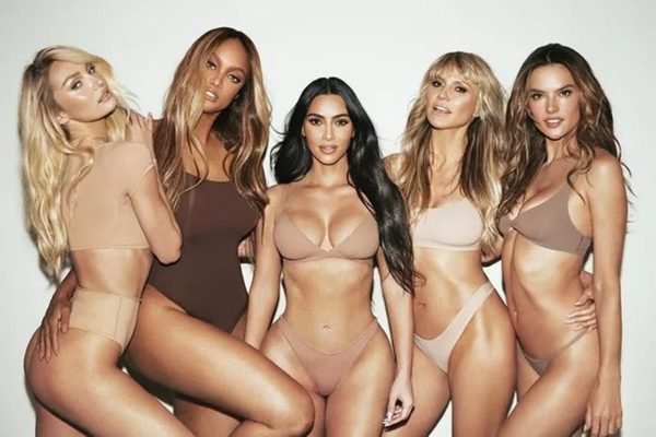 Cinco mulheres brancas posando para a câmera com lingeries, em fundo branco de estúdio