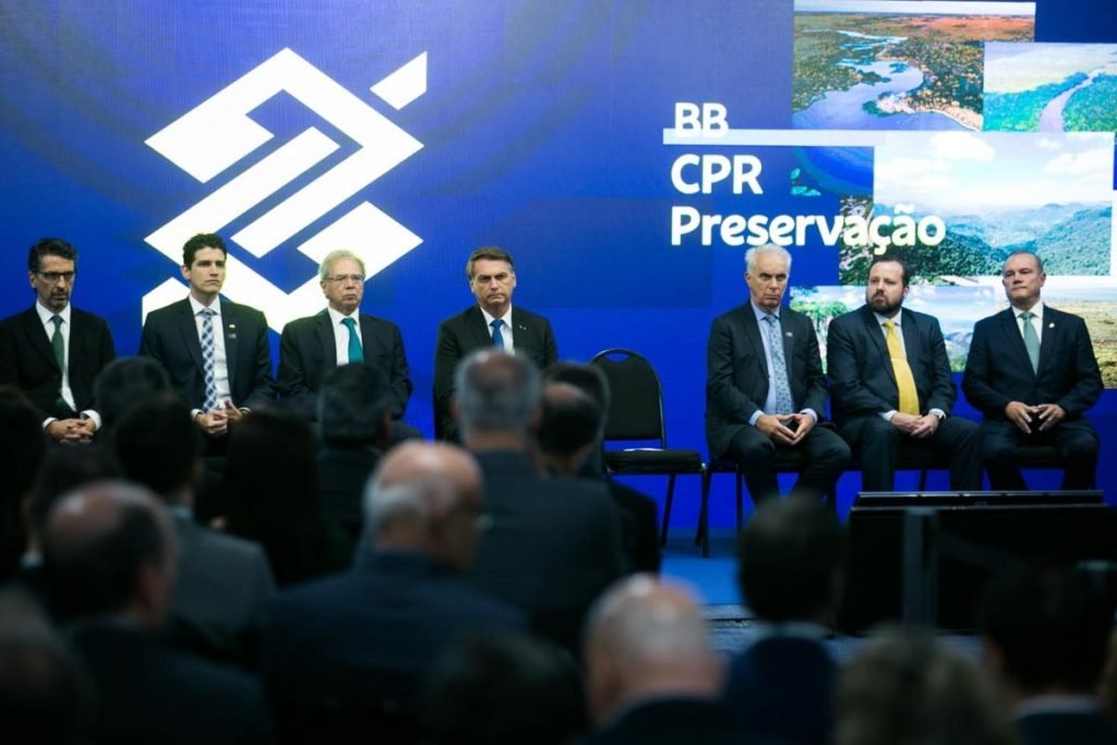 Presidente Bolsonaro participa do lançamento do programa do Banco do Brasil, Antecipa Frete. Ele está sentado ao lado do ministro Paulo Guedes e outras autoridades diante da plateia - Metrópoles