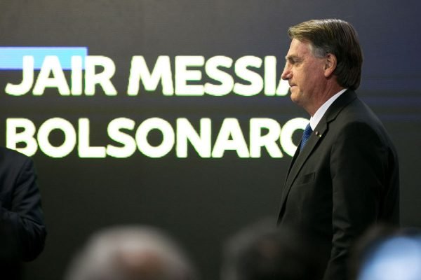 Presidente Bolsonaro participa do lançamento do programa do Banco do Brasil, Antecipa Frete. Ele está de lado, frente à plateia e ao painel com seu nome - Metrópoles