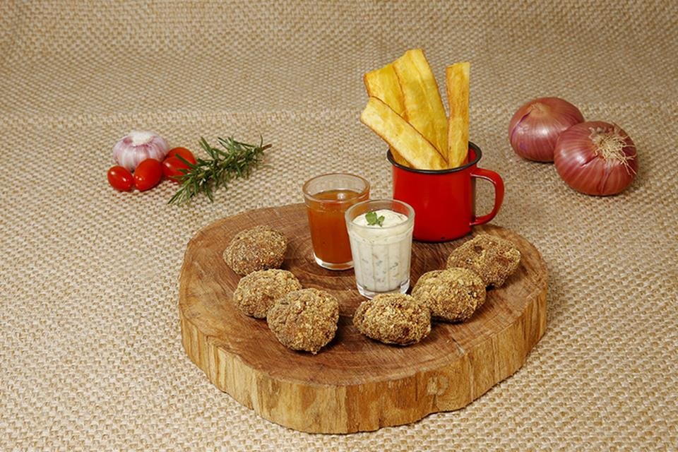 na foto vemos uma tabua de madeira com bolinhos e dois copinhos com molhos e uma xicara pequena com batatas fritas