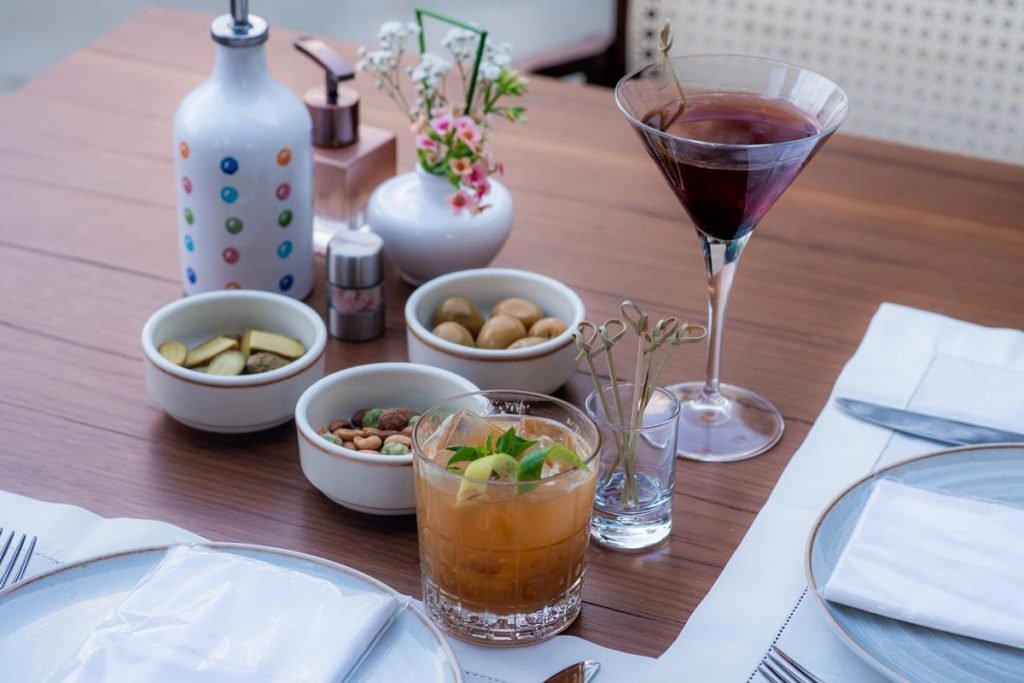 na foto vemos uma mesa de madeira com três cumbucas brancas com comidinhas dentro e copos com bebidas